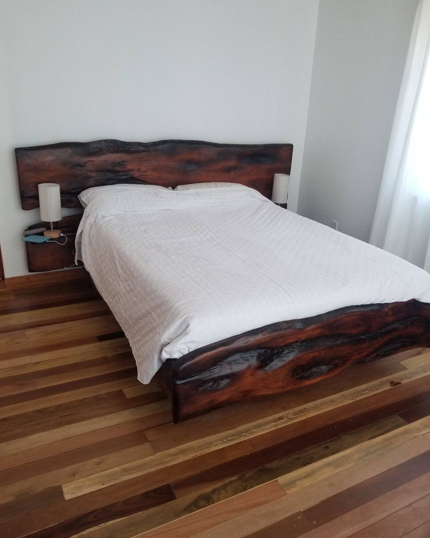 Queen bed with a dark live-edge hardwood slab headboard and branch side rails
