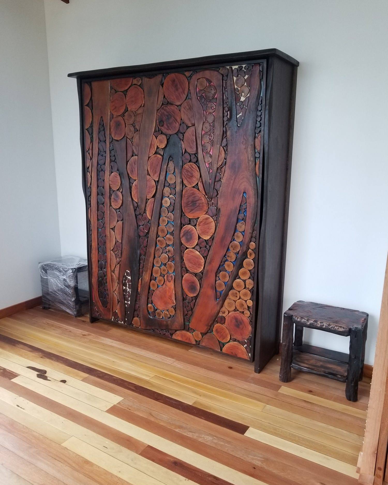Closed Murphy bed whose front is a mosaic of hardwood cross-sections and carved branch shapes set in coloured epoxy resin